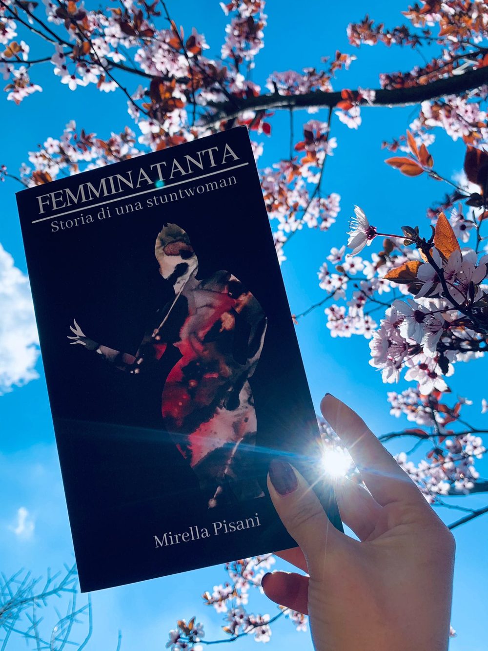 Il libro Femminatanta di Mirella Pisani tenuto in mano davanti a un albero in fiore e al cielo azzurro